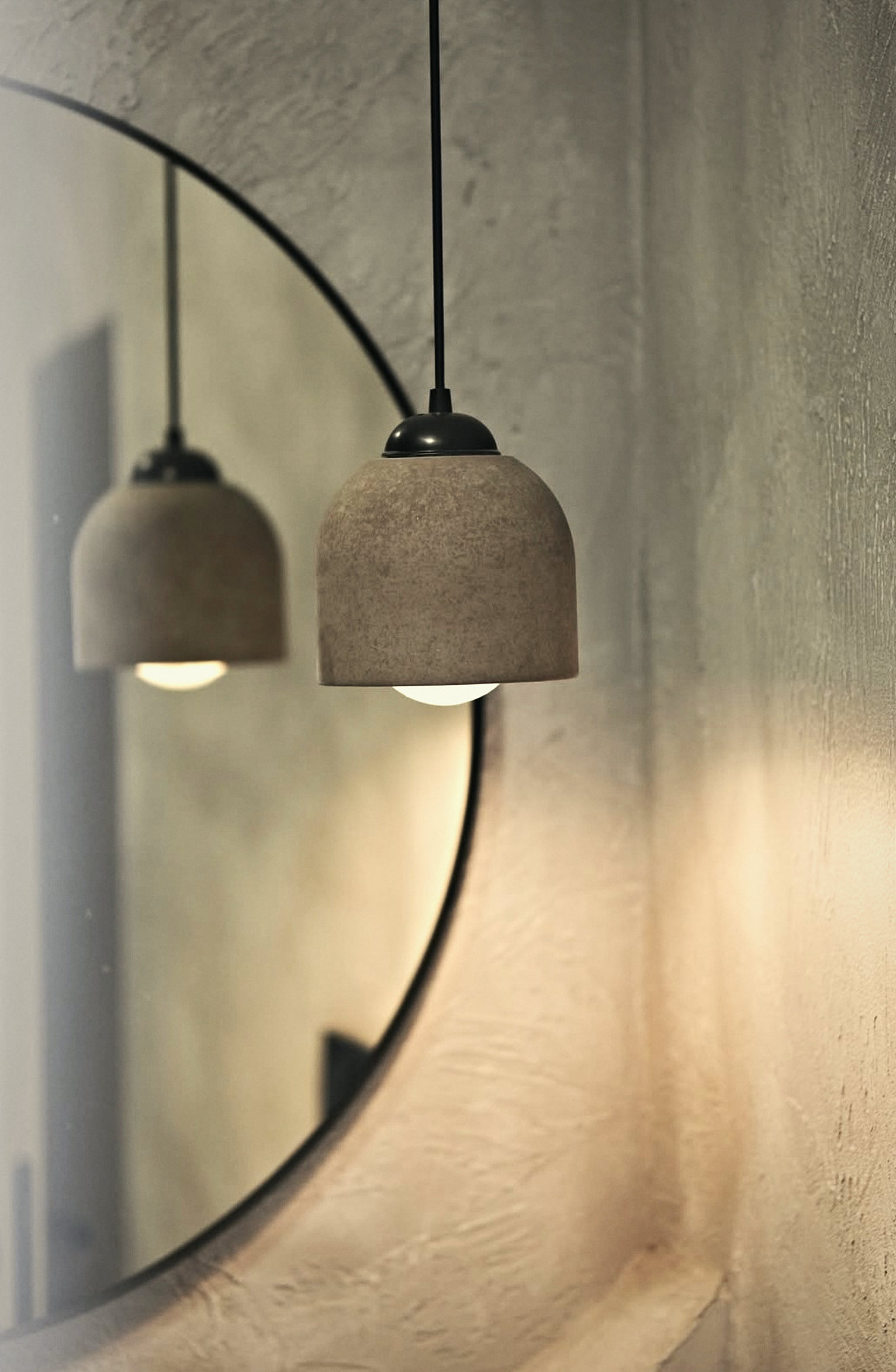 A stone pendant lamp reflected in a round black-framed mirror
